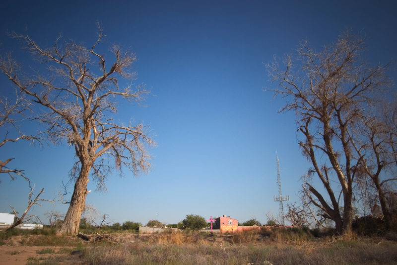 A cross stands in a cotton field in central Ciudad Juarez, Where the decomposing bodies of two women and the skeletal remains of six more were found. The lettering on the farm house in the background says, “A rural area were you can enjoy the tranquility of the outdoors in the heart of Cd. Juarez. “ September 21, 2005 Photo by Christ Chavez